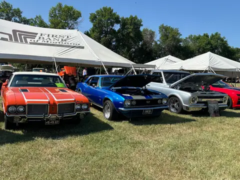 Classic cars are parked on grass in front of white tents.