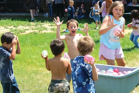 Children playing with water balloons outdoors on a lawn.