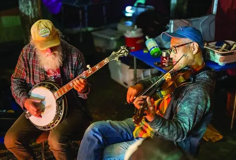 Two men playing a banjo and a violin outdoors at night.