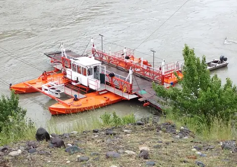 An orange and white ferry on a river next to a rocky bank.