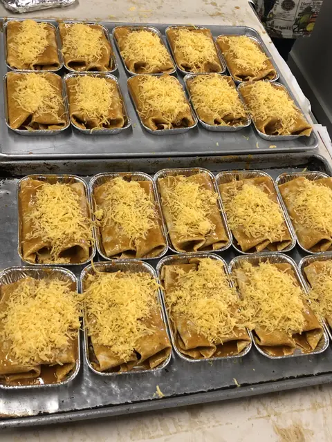 A high angle shot of foil trays filled with enchiladas topped with cheese.