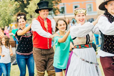 People in traditional costumes and casual clothes holding hands and dancing outdoors.