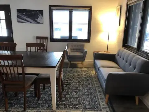 An interior view of a living and dining area with a dining table, chairs, sofa, and armchair.
