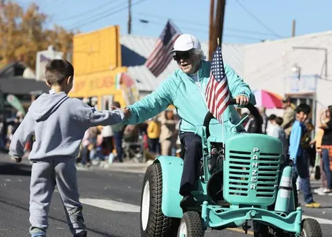 A person driving a small tractor high-fives a child on a street.