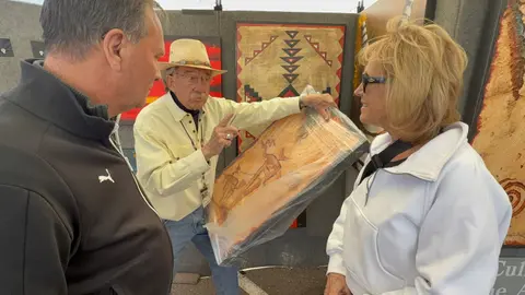 An artist shows a framed artwork to two people at an art show.