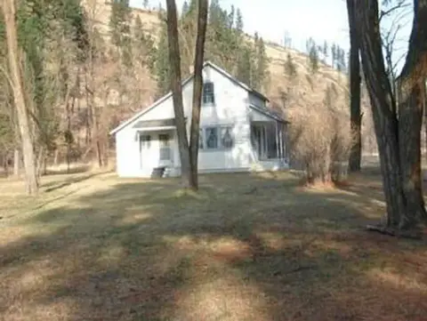 A white house stands in a grassy area surrounded by trees and a hillside.