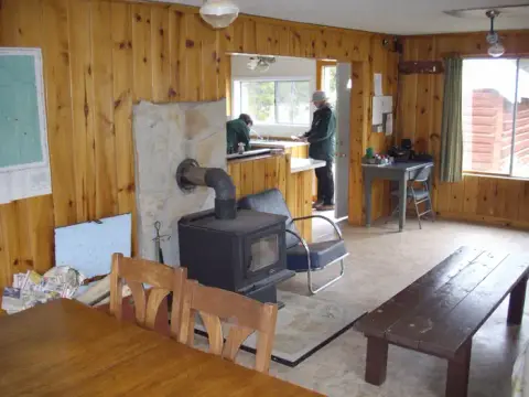 The interior of a wooden cabin features a wood-burning stove and wooden furniture.