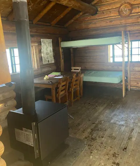 Interior of a rustic log cabin with bunk beds and a wood stove.