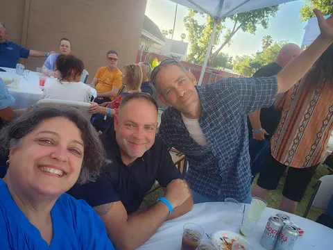 A group of people sitting at a table outdoors and smiling at the camera.