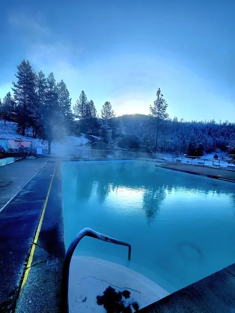 An outdoor swimming pool surrounded by snowy trees and mountains at sunrise.
