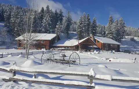 A snow-covered log lodge and surrounding landscape with an old farm implement in the foreground.