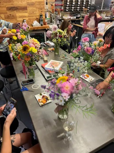 People arrange flower bouquets at a long table indoors.