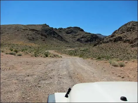 A dirt road winds through a desert landscape with mountains under a clear blue sky.