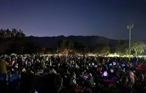 A large crowd gathered at night outdoors with mountains in the background.