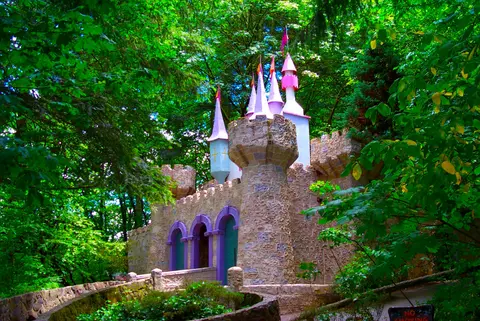 A stone castle with pink spires is nestled among lush green trees.
