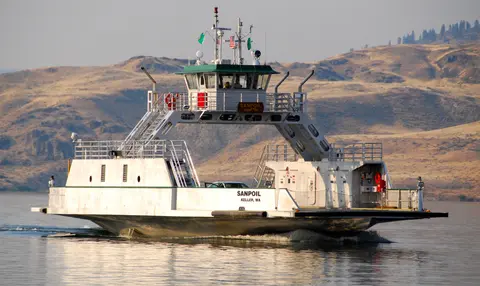 A ferry boat travels across a body of water with hills in the background.