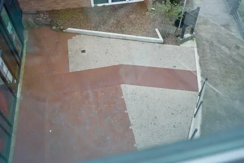An overhead view of an outdoor paved courtyard with red and light gray bricks.