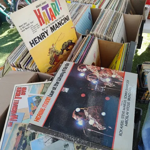 A photograph showing various vinyl record albums in boxes at an outdoor market.
