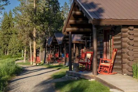 A row of wooden cabins with red rocking chairs on their porches along a path.