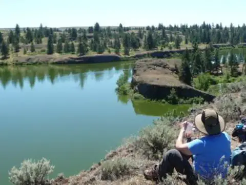 A person sitting on a cliff overlooking a lake and surrounding landscape.