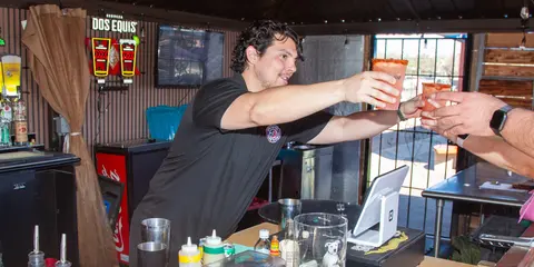 A bartender handing drinks to a customer across a bar.
