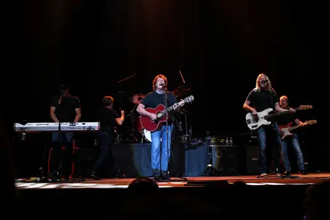 A band performs on stage with instruments in a dark venue.