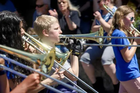 A group of young musicians play trombones outdoors.
