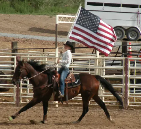 A person rides a horse while carrying an American flag in an arena.