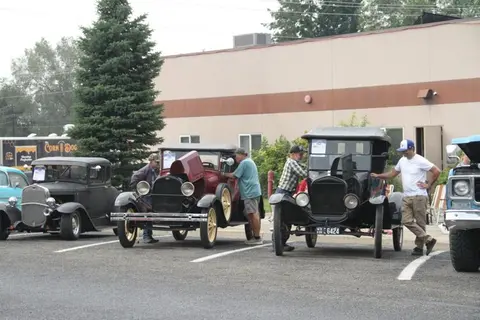 Several classic cars are parked in a row with people standing near them.