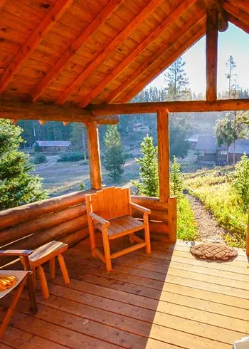 A wooden cabin porch overlooking a forest landscape.