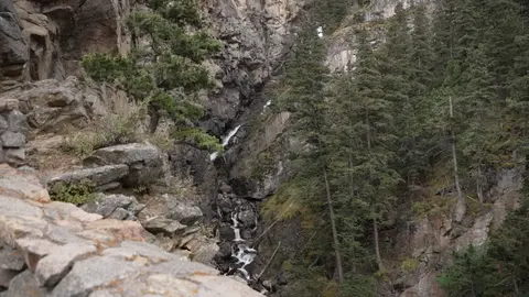 A small waterfall flowing down a rocky, forested canyon.