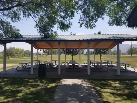 A covered picnic pavilion sits in a park with green fields in the background.