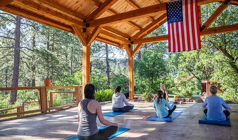 People practice yoga on mats under a wooden pavilion outdoors.