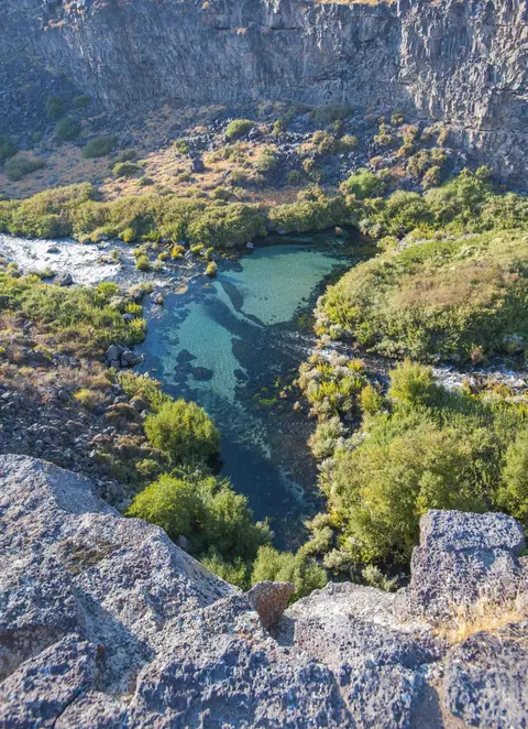 A high-angle view of a clear blue stream winding through a rocky canyon with green vegetation.