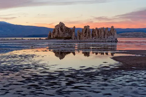 Tufa towers rise from shallow water under a colorful sunset sky.
