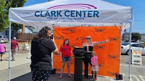 A person takes a photo of three people posing in front of a festival backdrop.