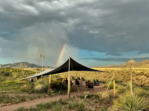 A shaded seating area outdoors under stormy skies with a rainbow in the distance.