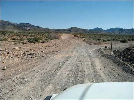 A dirt road winding through a desert landscape with mountains in the background.
