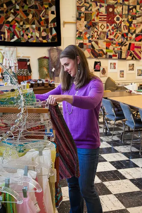 A woman browses through clothing racks inside a shop with quilts on the walls.