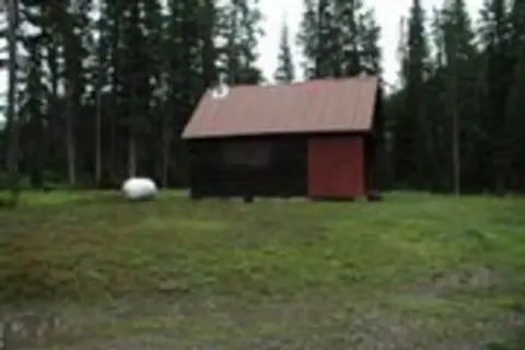 A small cabin stands in a clearing surrounded by trees.