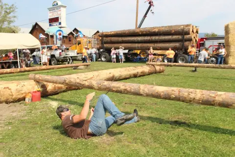 A man falls backward while participating in an outdoor event with logs.