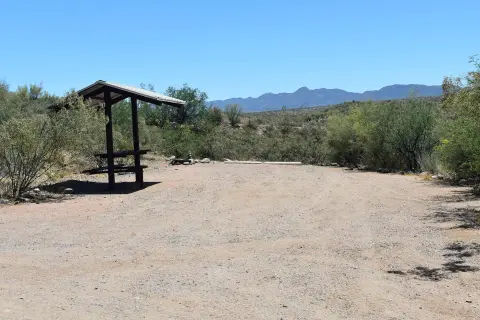 An outdoor picnic shelter and parking space in a desert landscape with mountains in the background.