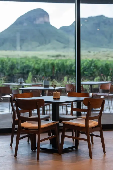 An indoor view of tables and chairs with a mountain landscape visible through a large window.