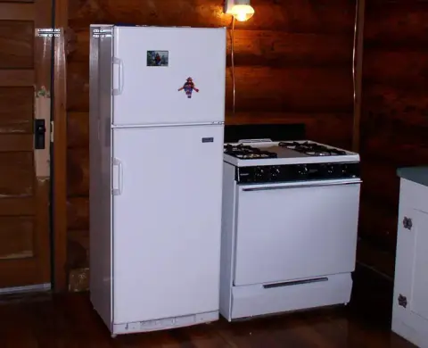 A white refrigerator and stove stand side by side in a rustic log cabin kitchen.