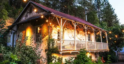 An old rustic stone and wood building lit up by string lights at dusk.
