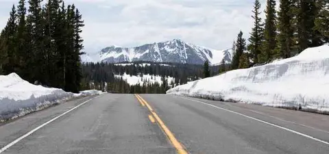 A road cutting through a snowy mountainous landscape with pine trees.