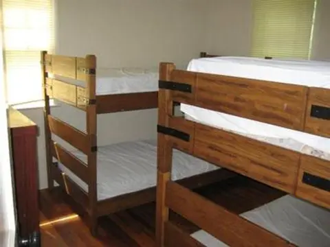 Two wooden bunk beds in a room with a hardwood floor and windows.