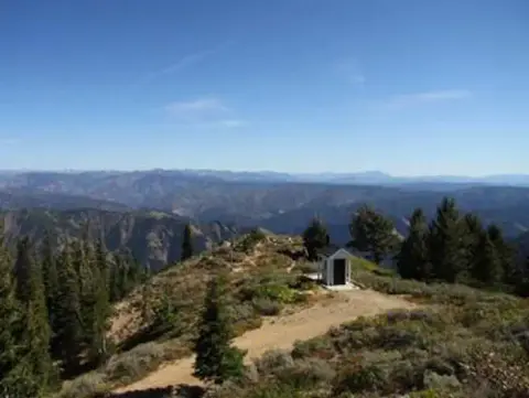A small structure sits atop a mountain ridge with expansive views.