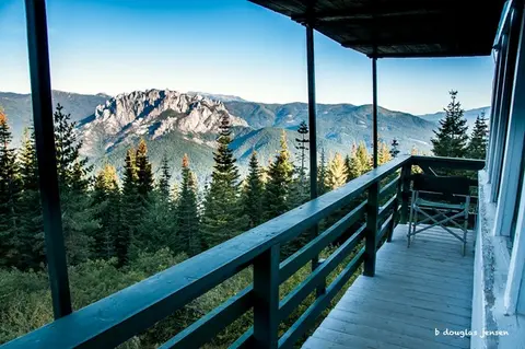 A scenic view of a mountain range and pine forest from a wooden balcony.