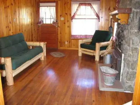 Interior of a wood-paneled room with rustic furniture and a stone fireplace.